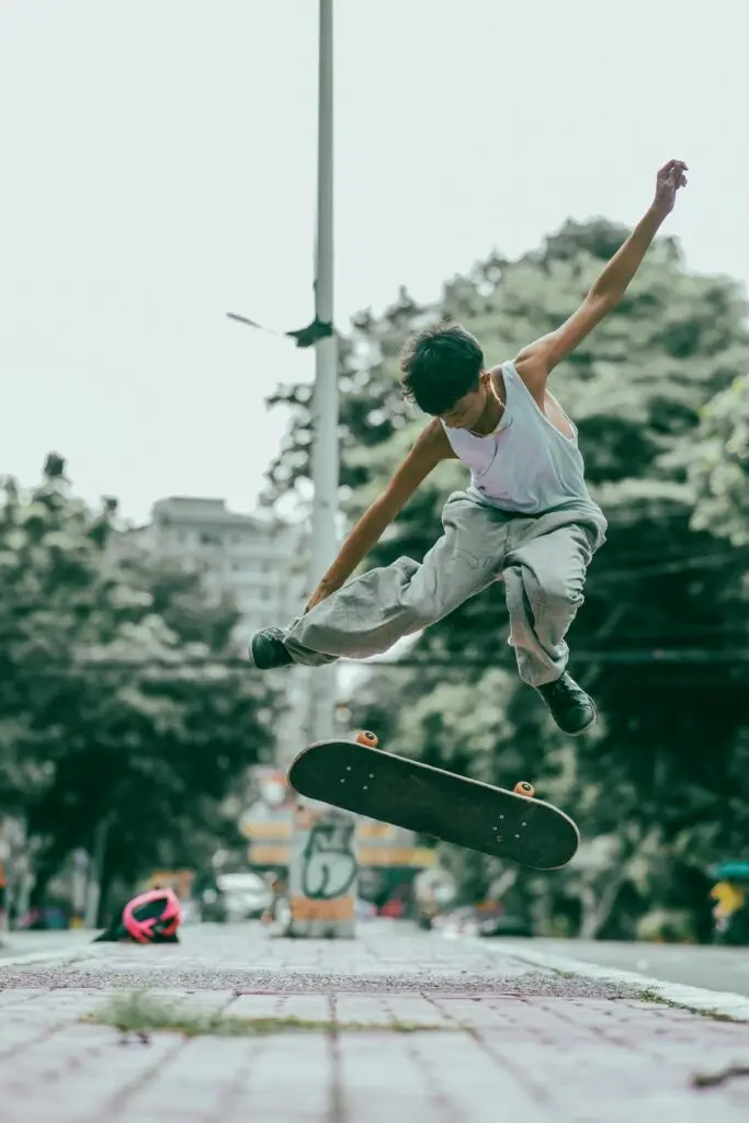 Dynamic action shot of a young man executing a skateboard trick with trees and urban background.